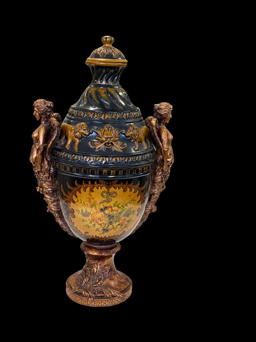 Neoclassical Style Lidded Urn w/ Angels: This ornate neoclassical style lidded urn features a dark glazed body with a central hand-painted cartouche of musical instruments and floral motifs. The piece is flanked by two large bronzed figures 