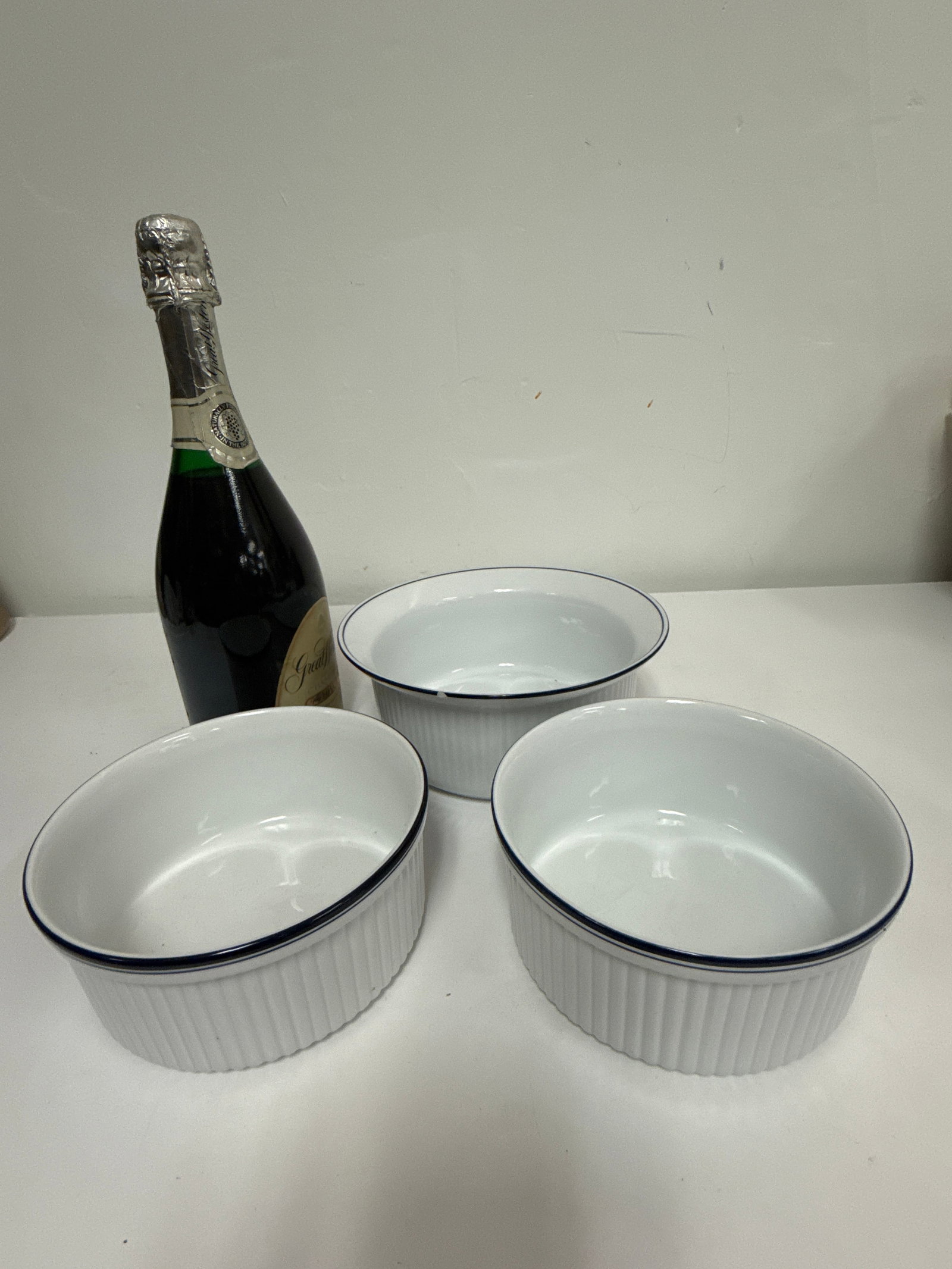3pc Dansk Bistro Blue Rim Serving Bowls: This set of three Dansk Bistro porcelain bowls features a classic white ribbed design accented with a dark navy blue rim. The collection includes two straight-sided ramekin-style bowls and one larger