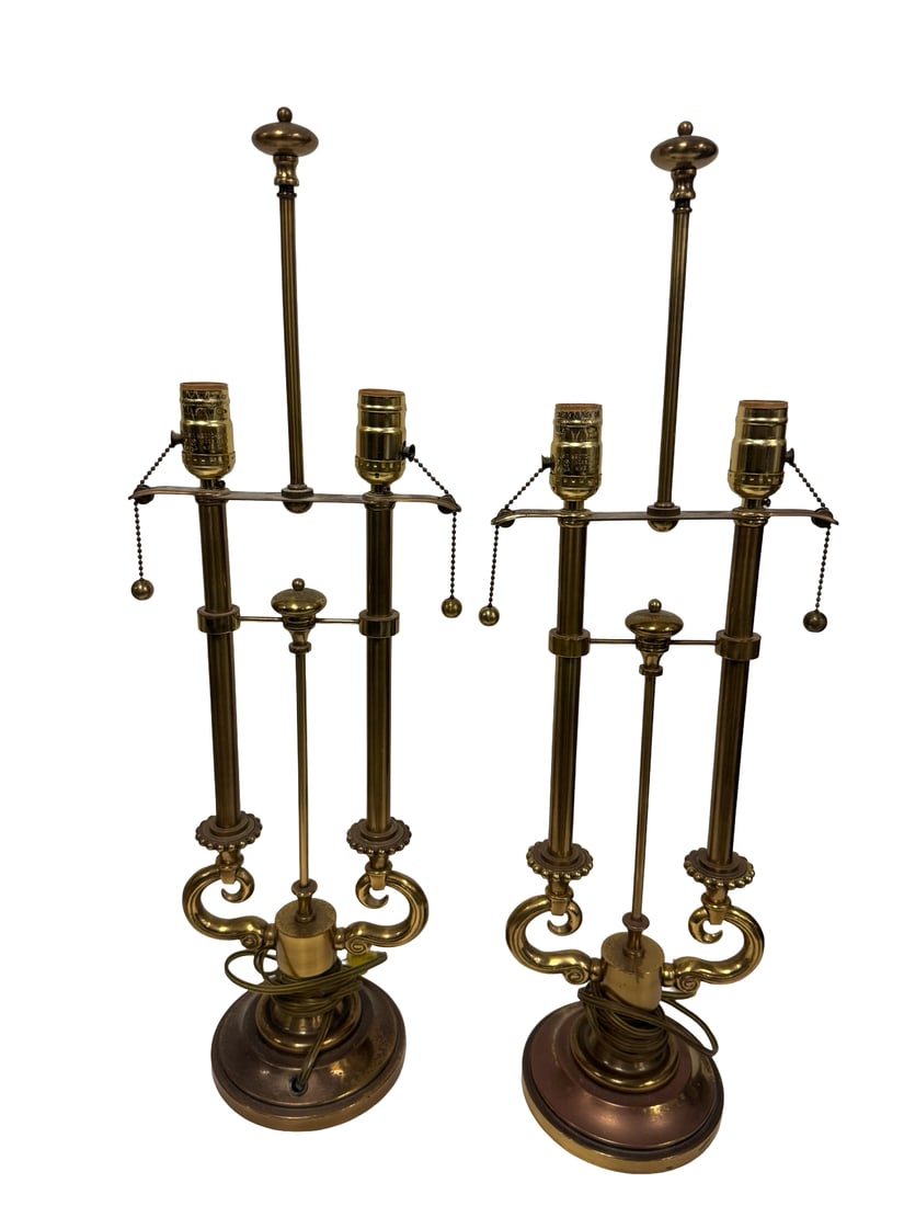 Pair of Vintage Neoclassical Brass Lamps: This pair of vintage brass table lamps features a tall, slender design with scrolled accents nearing the circular bases. Each lamp is equipped with a dual socket cluster and pull-chain switches,