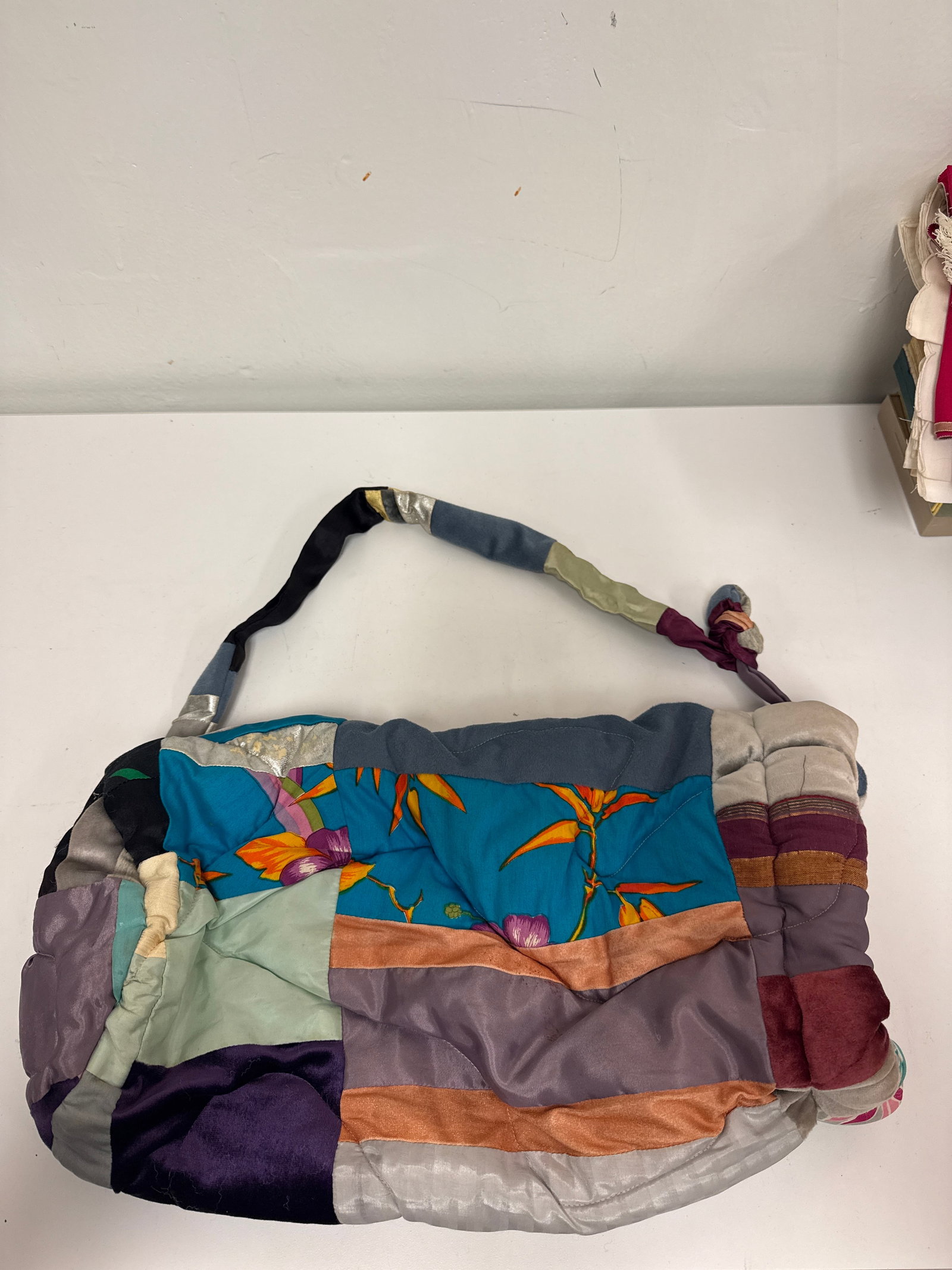 Eclectic Mixed Textile Patchwork Bag: This large patchwork hobo-style shoulder bag features an eclectic mix of multi-textured fabrics including velvet, silk-like synthetics, and floral prints. The bag is designed with a soft, padded