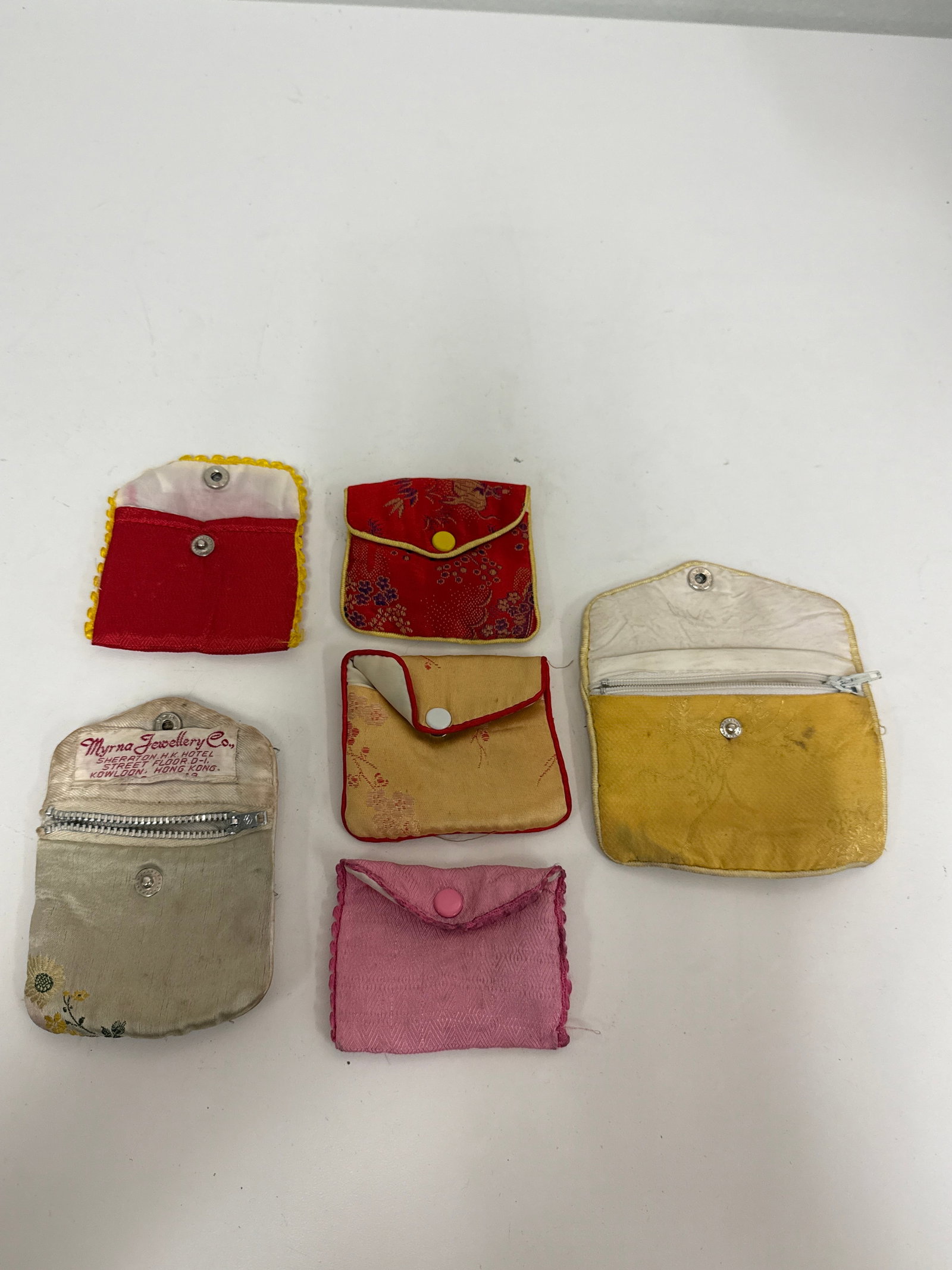 Group of 6 Vintage Asian Fabric Pouches: This collection includes six vintage fabric jewelry pouches featuring various Asian-inspired patterns and damask weaves. One pouch prominently displays a Myrna Jewellery Co. label from Kowloon, Hong K