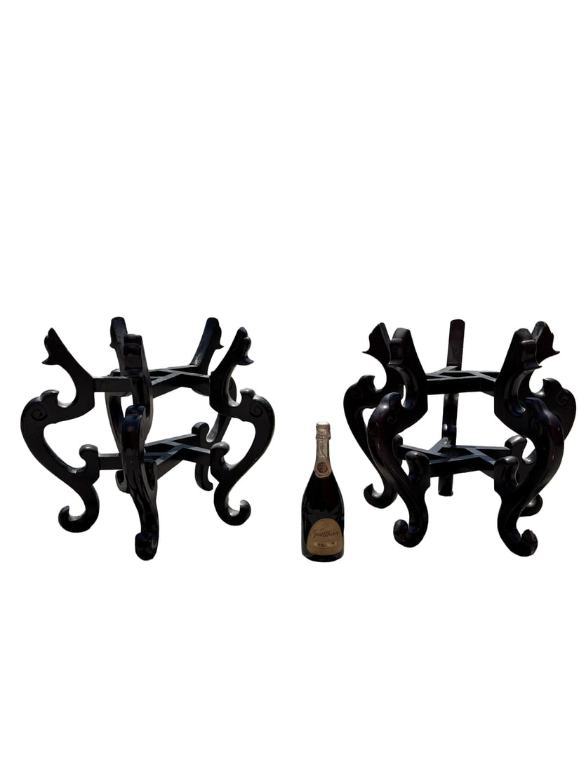 Pair of Chinese Style Ebonized Stands: This pair of black-lacquered wooden stands features elaborate scrollwork in a traditional Chinese style. Each piece is designed with four integrated legs and cross-stretcher supports to accommodate la