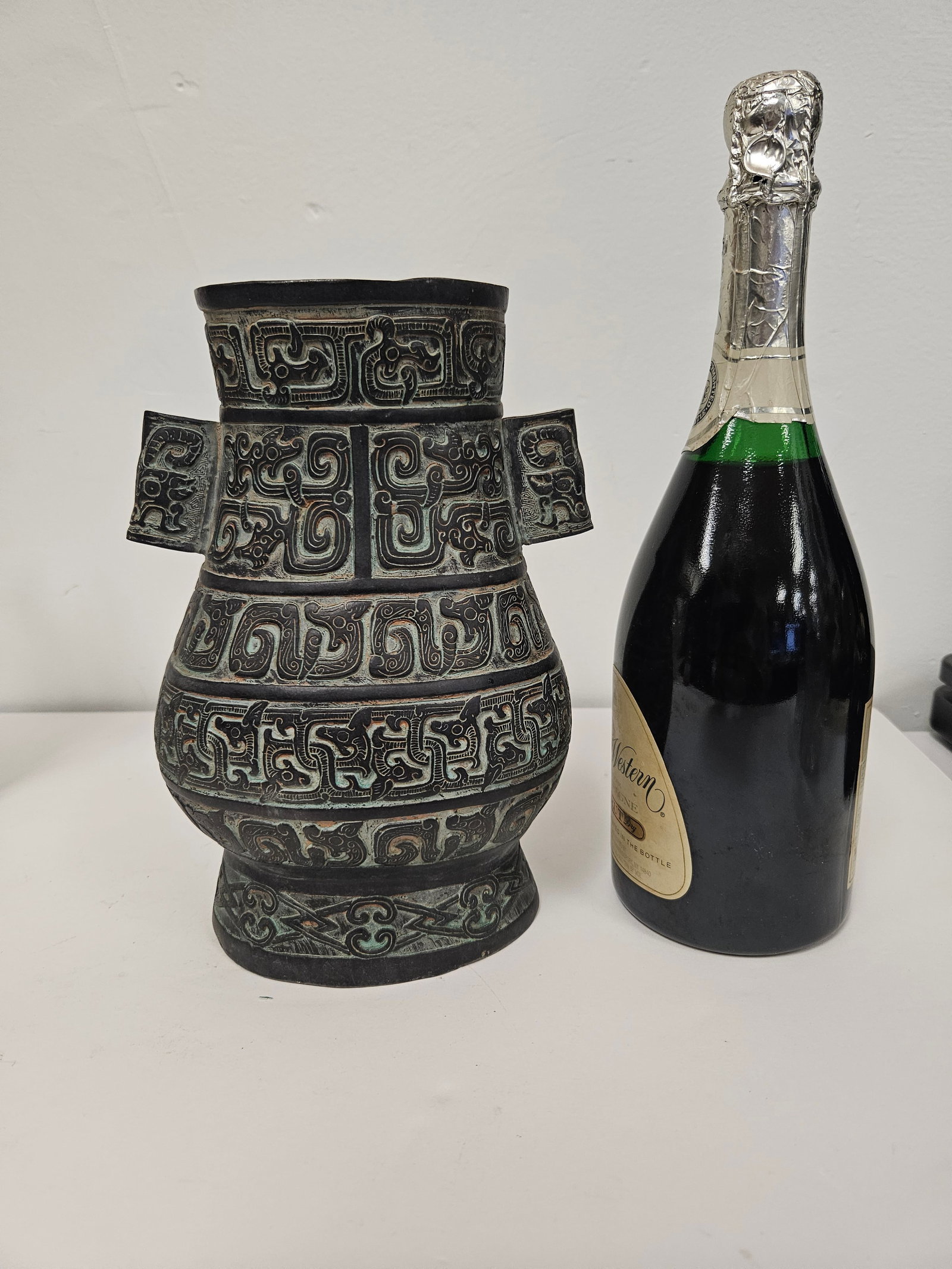 Archaic Style Chinese Bronze Ritual Hu: This bronze ritual vessel is designed in the archaic Hu style, featuring intricate relief carvings of taotie masks and geometric scrolling. The vessel is accented with dual flat handles and a tapered 