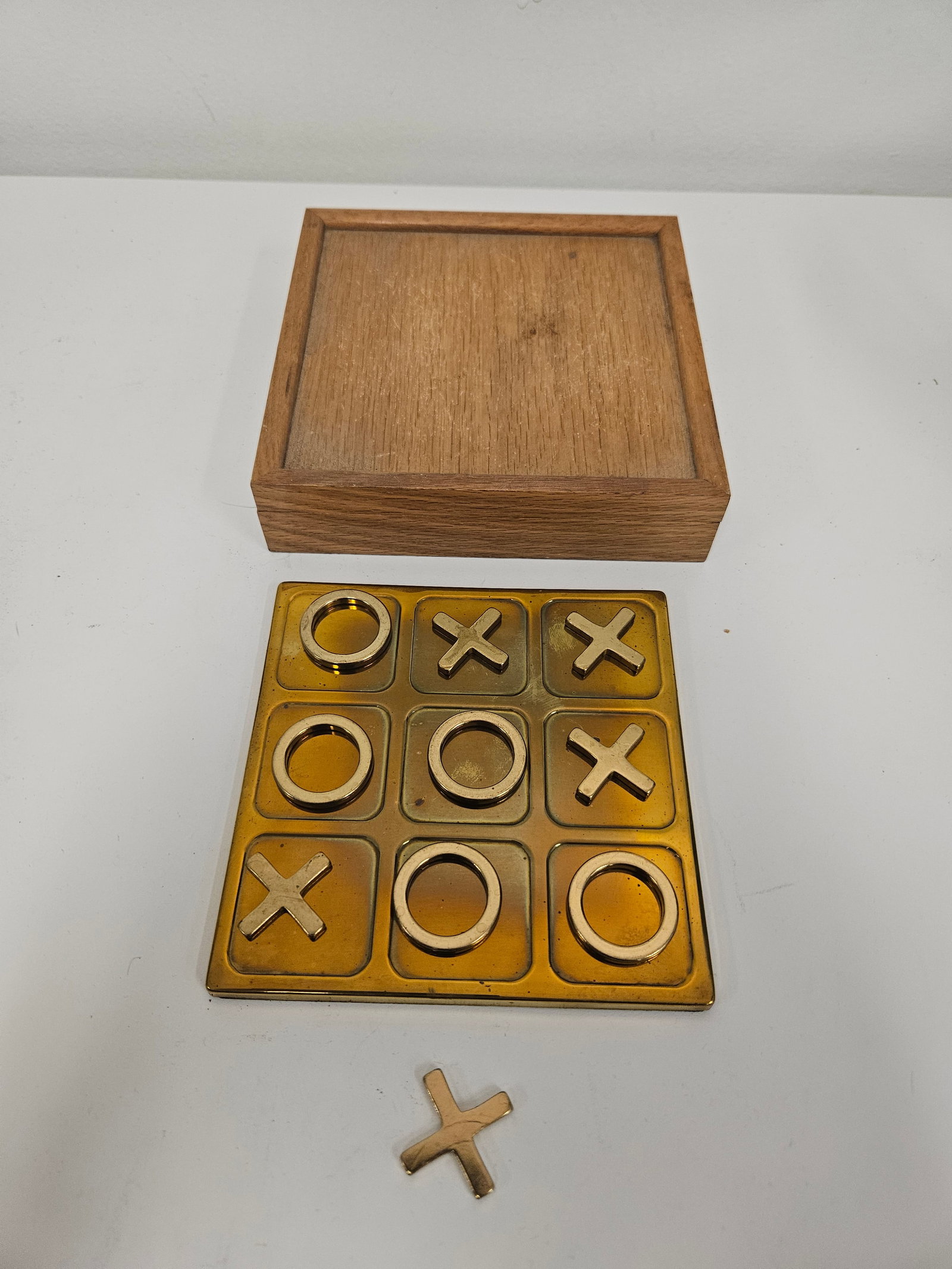 Vintage Style Brass-Tone Tic-Tac-Toe Set: This vintage-style tic-tac-toe set features a heavy brass-tone game board and polished metal X and O playing pieces. The set is housed in a square decorative wooden box with a hinged lid and felt-line