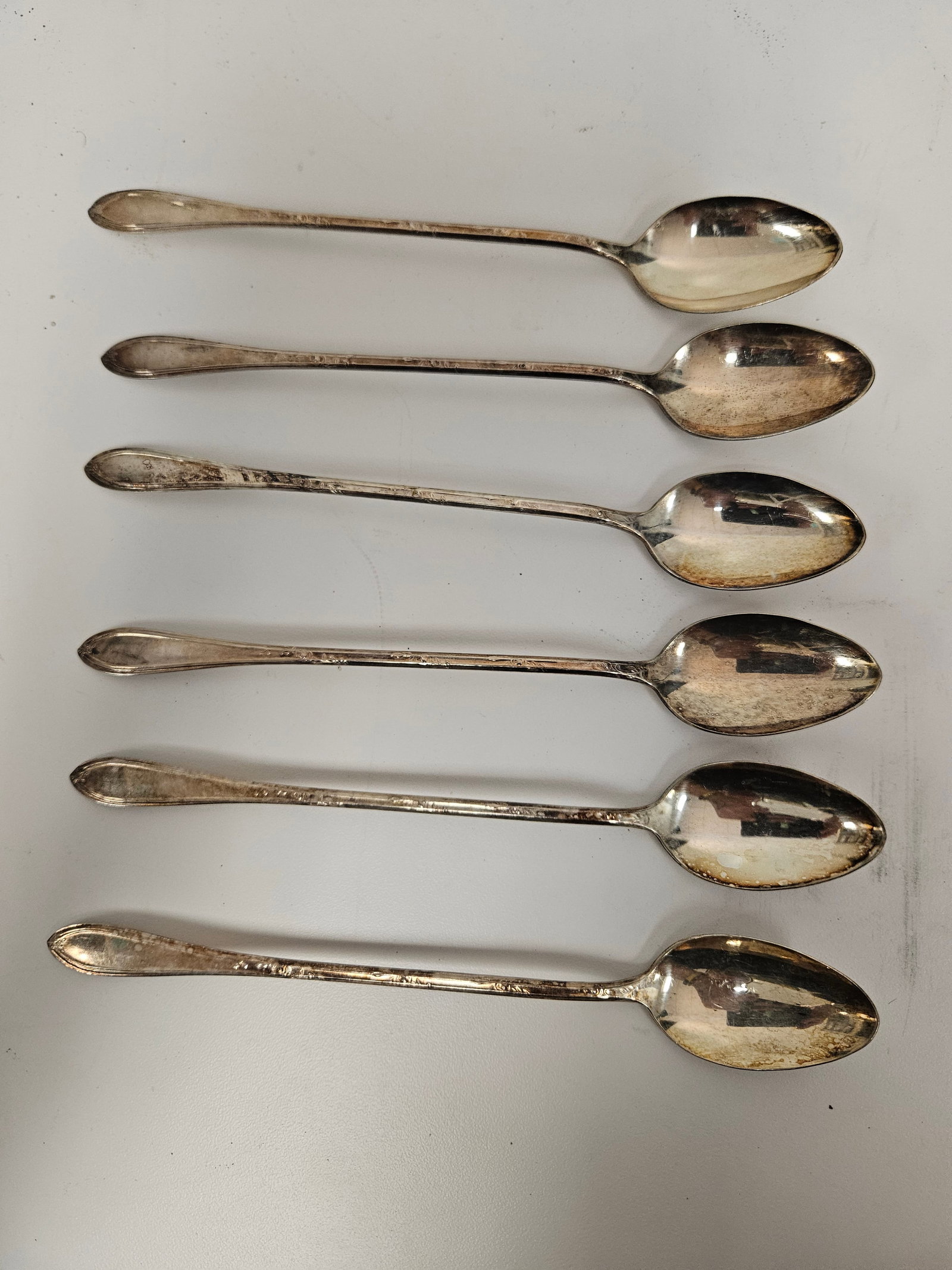 Set of 6 Floral Silver-Plated Tea Spoons: This set includes six matching silver-plated iced tea spoons featuring long, slender stems decorated with delicate floral and leaf engravings. The elegant pattern extends down the handles, terminating