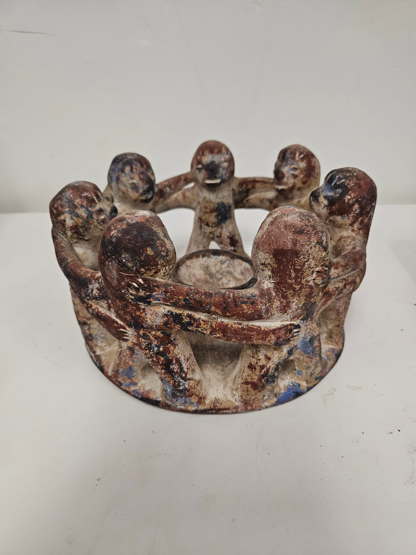 Terracotta Circle of Friends Candle Hold: This Terracotta Circle of Friends candle holder features eight interconnected figures representing friendship and unity. The piece displays a rustic, multi-toned finish with earthy red and blue