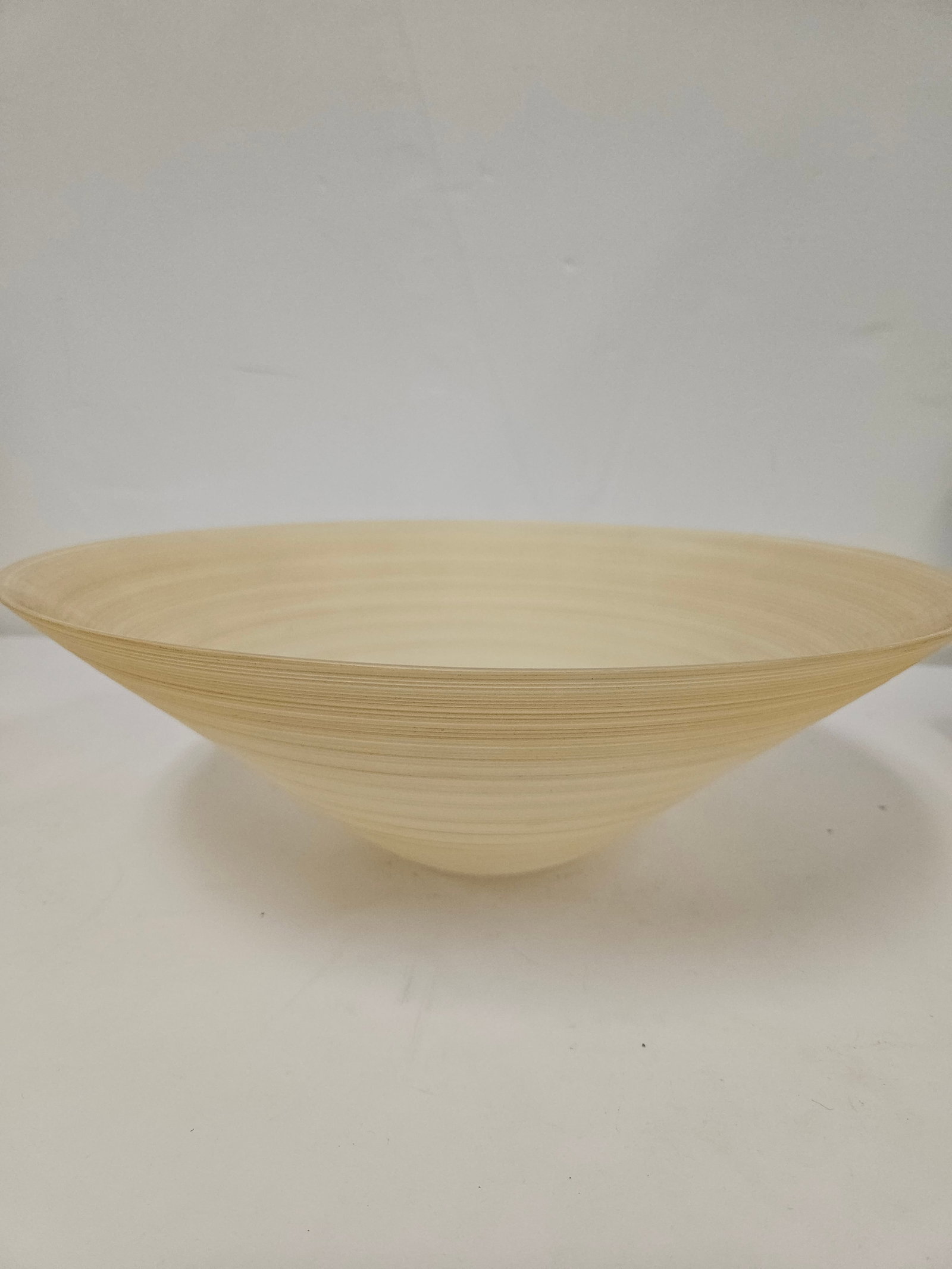 Contemporary Spun Bamboo Bowl: This contemporary bowl is constructed from spun bamboo, featuring a natural light wood tone with visible concentric grain patterns. The bowl has a deep conical shape and a smooth interior finish that
