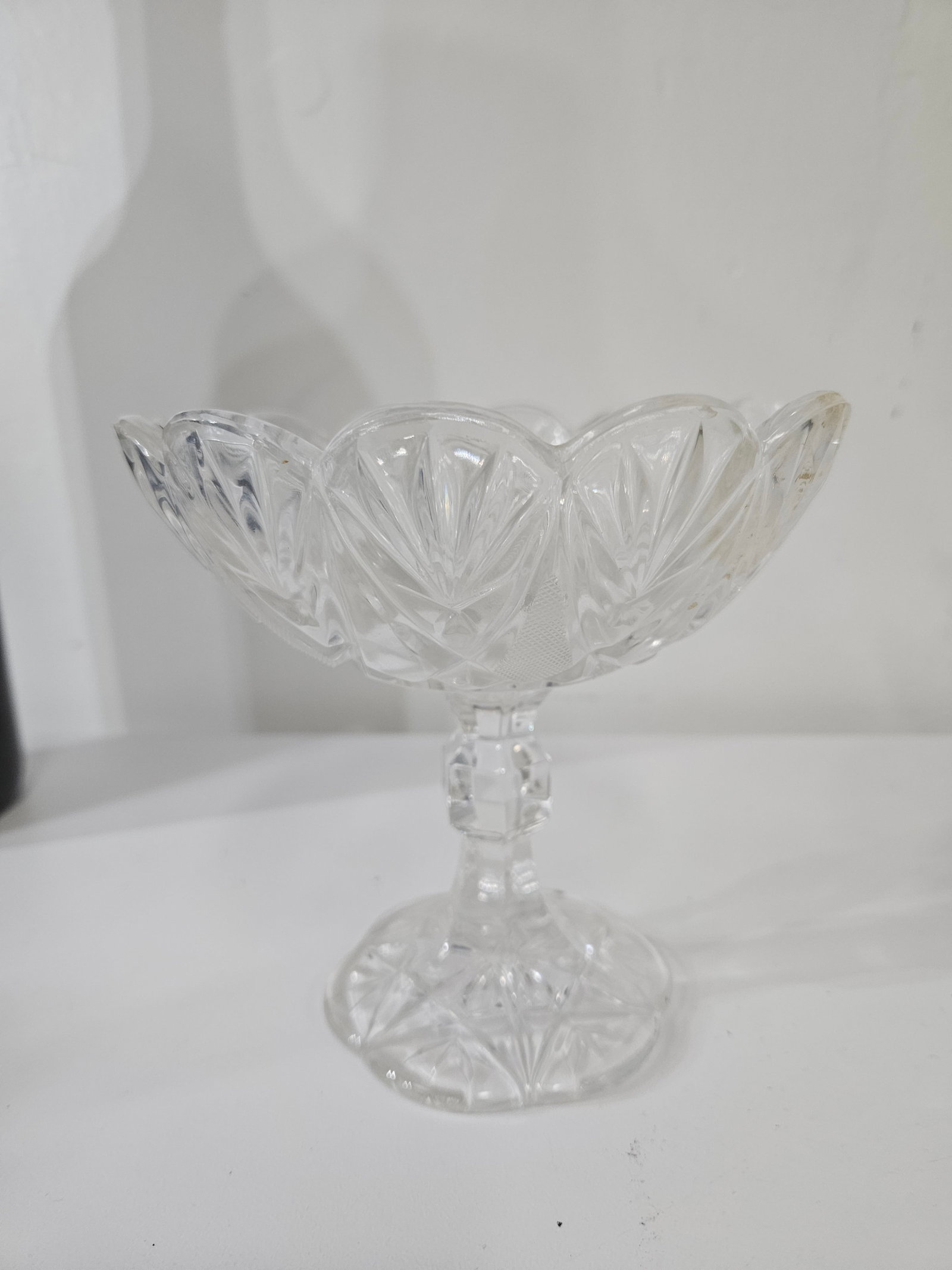 Vintage Pressed Glass Footed Candy Bowl: This elegant footed candy dish is crafted from clear pressed glass featuring a classic sunburst and fan motif. It stands on a faceted stem with a wide, scalloped rim bowl and a matching decorated