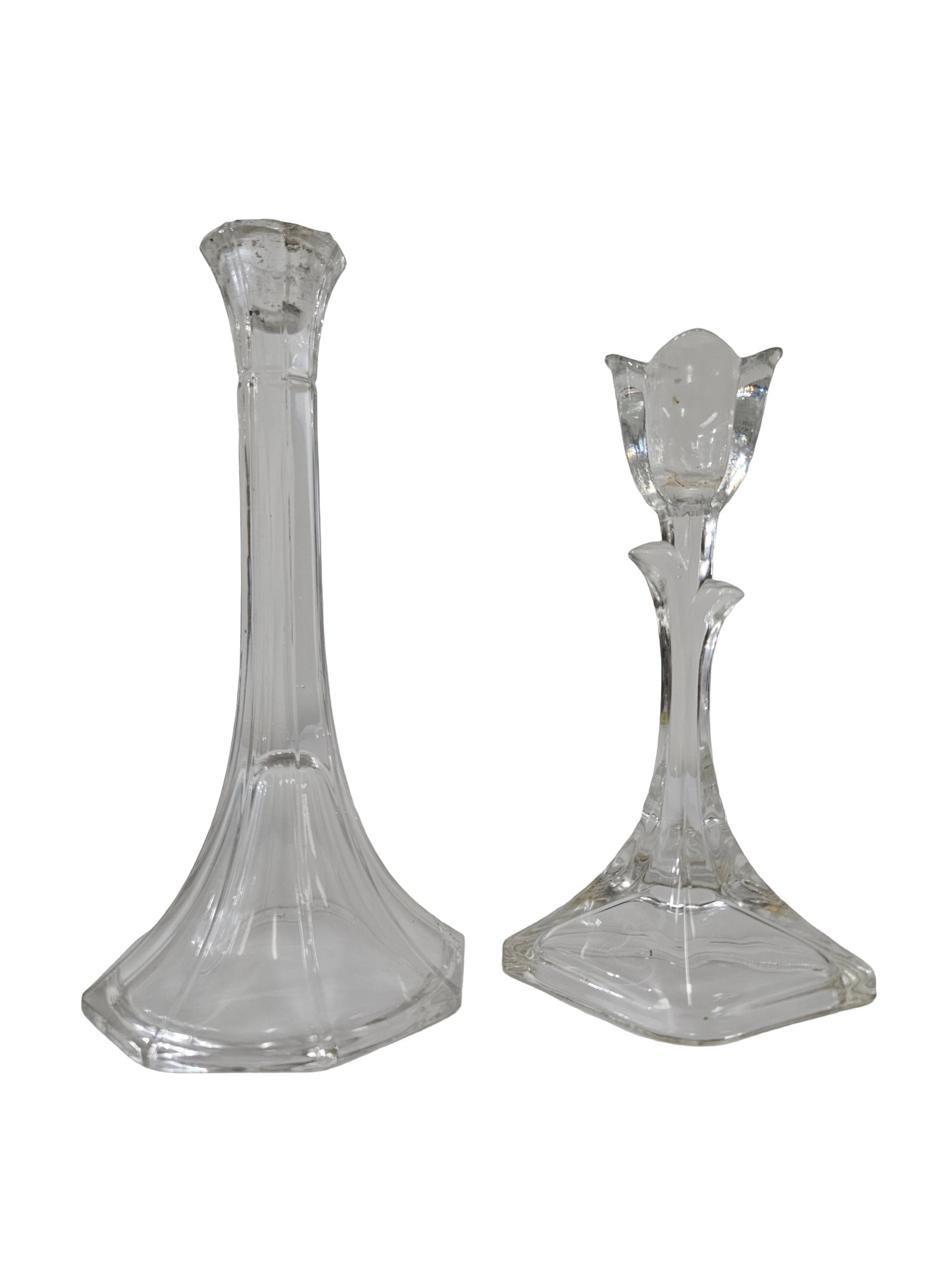 2 Clear Glass Tabletop Candlesticks: This pair of clear glass candlesticks features two distinct and elegant designs. One holder is crafted in the shape of a blooming tulip atop a decorative stem and square base, while the other