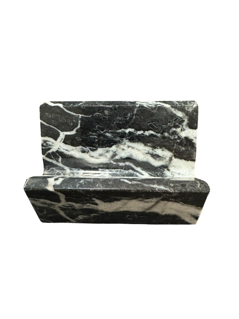 Polished Black Marble Card Holder: This elegant business card holder is crafted from a solid block of polished black and white veined marble. The minimalist design features a simple angled slot to hold cards securely on a desk or count