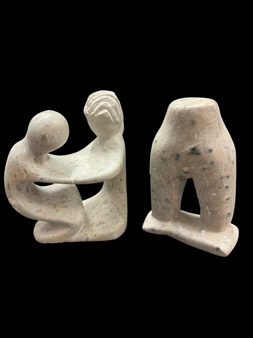 Pair of Hand-Carved Stone Sculptures: This pair of hand-carved stone sculptures features stylized figurative forms in a light-colored, speckled soapstone. One piece depicts a kneeling mother and child in an intimate embrace, while the sec