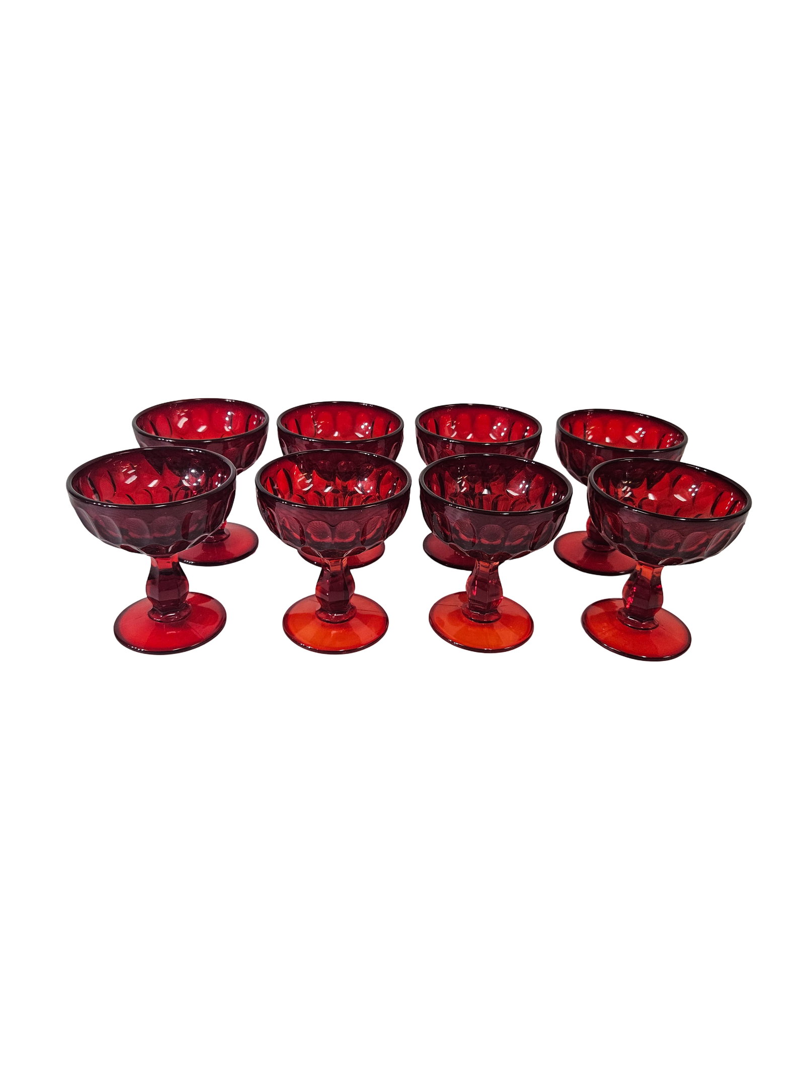 Eight Vintage Ruby Red Thumbprint Bowls: A service of eight vintage ruby red pressed glass dessert bowls in a classic thumbprint pattern. Each piece features a short faceted stem and a wide circular foot with a deep, vibrant red hue. This co