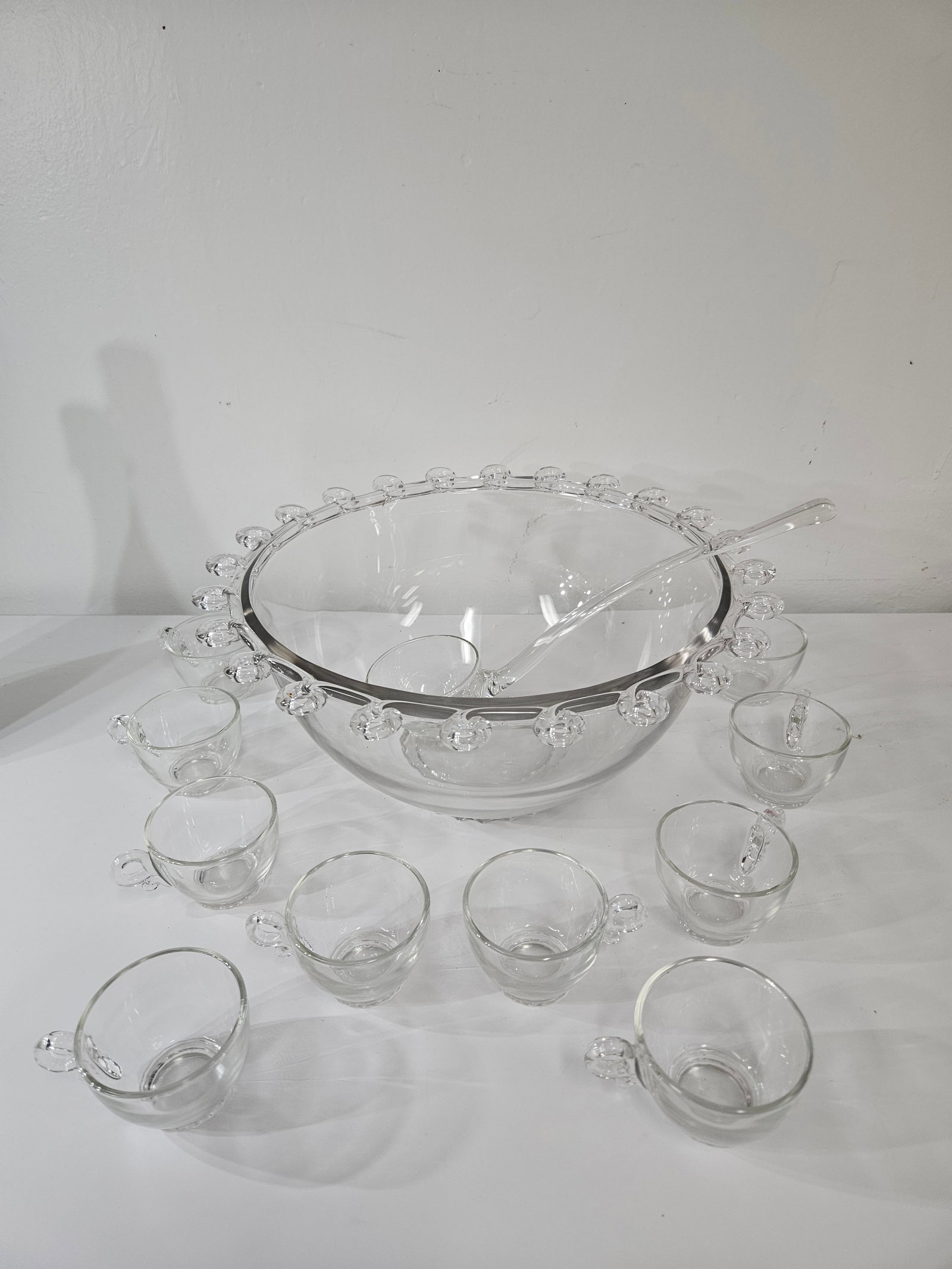Vintage Beaded Rim Glass Punch Bowl Set: This vintage glass punch set features a large serving bowl with a distinctive Boopie-style beaded rim. The set includes a matching glass ladle and ten handle cups with textured circular bases. The