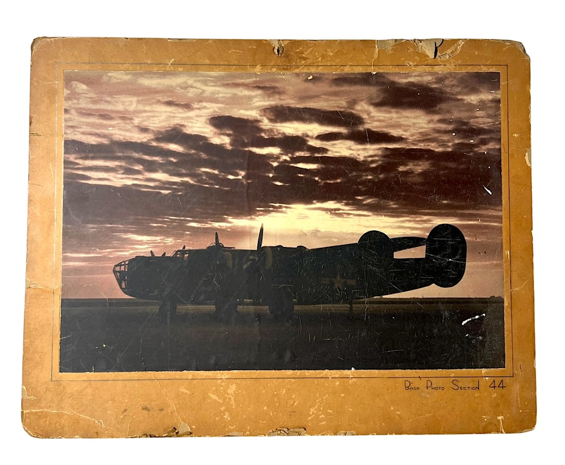 WWII Bomber Silhouette Photograph: Large mounted sepia photograph of a multi-engine military bomber silhouetted at sunset, marked "D.B. Base Photo Section 44". Worn mount with scratches, edge losses, and age wear.