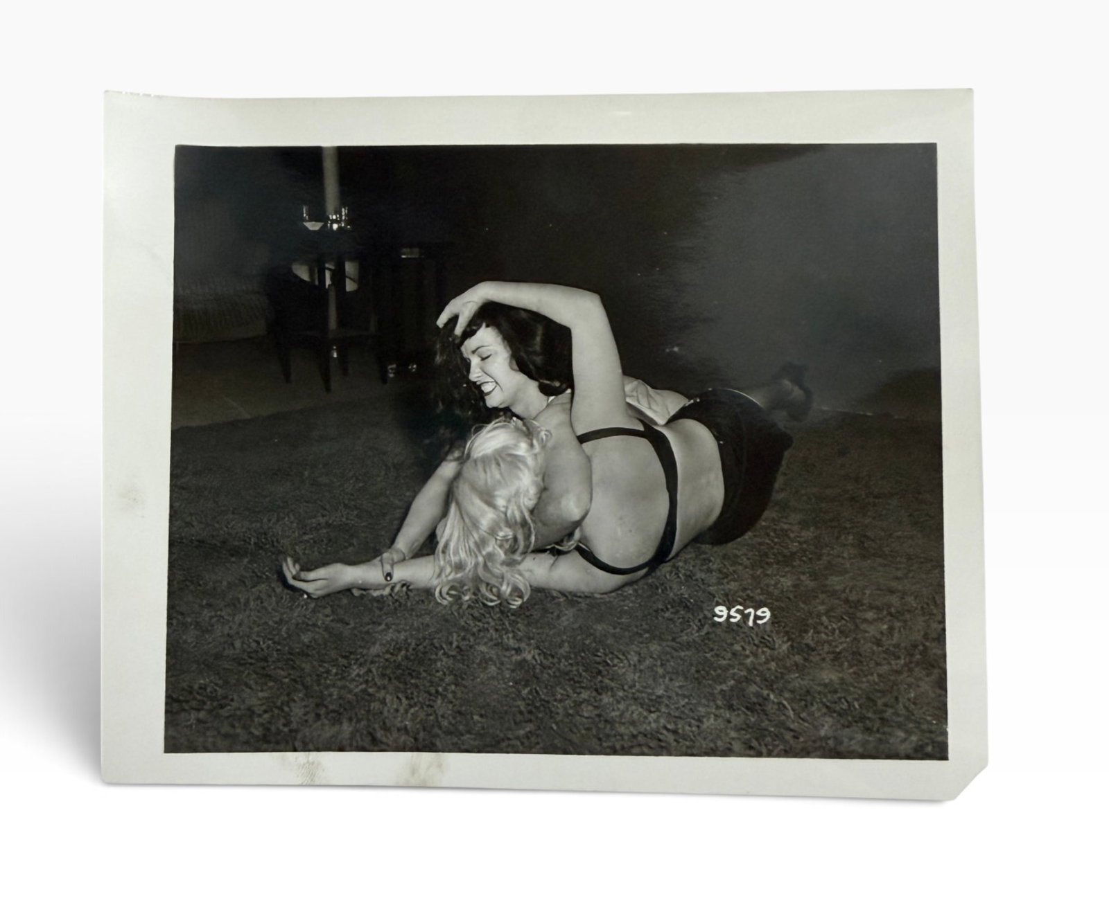 Vintage BlackandWhite Adult Nude Photograph Bettie Page: Original vintage black-and-white glossy photograph depicting a staged adult scene. Image bears production/reference number 9579. Age-related handling and surface wear.