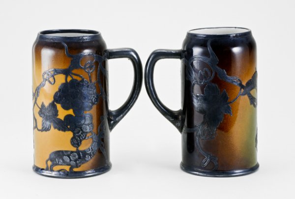 Early Lenox Silver Overlay Steins: Both measure 7 1/8" tall, pottery stein with Sterling? overlay in a nouveau pattern. One has a section of silver missing.