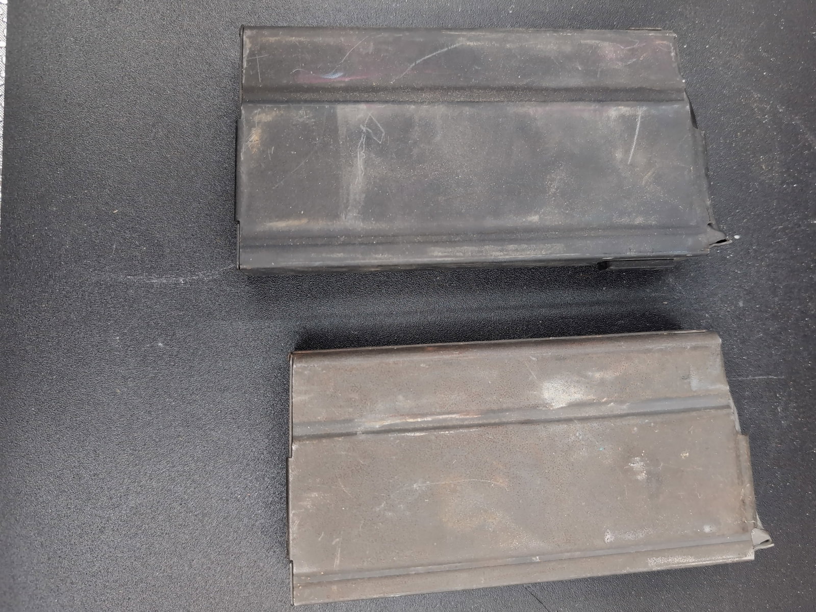 Pair of M14 Rifle Magazines: A set of two metal box magazines designed for the M14 rifle platform. The items feature a standard steel construction with a dark finish. The magazines exhibit surface wear, scratches, and oxidation c