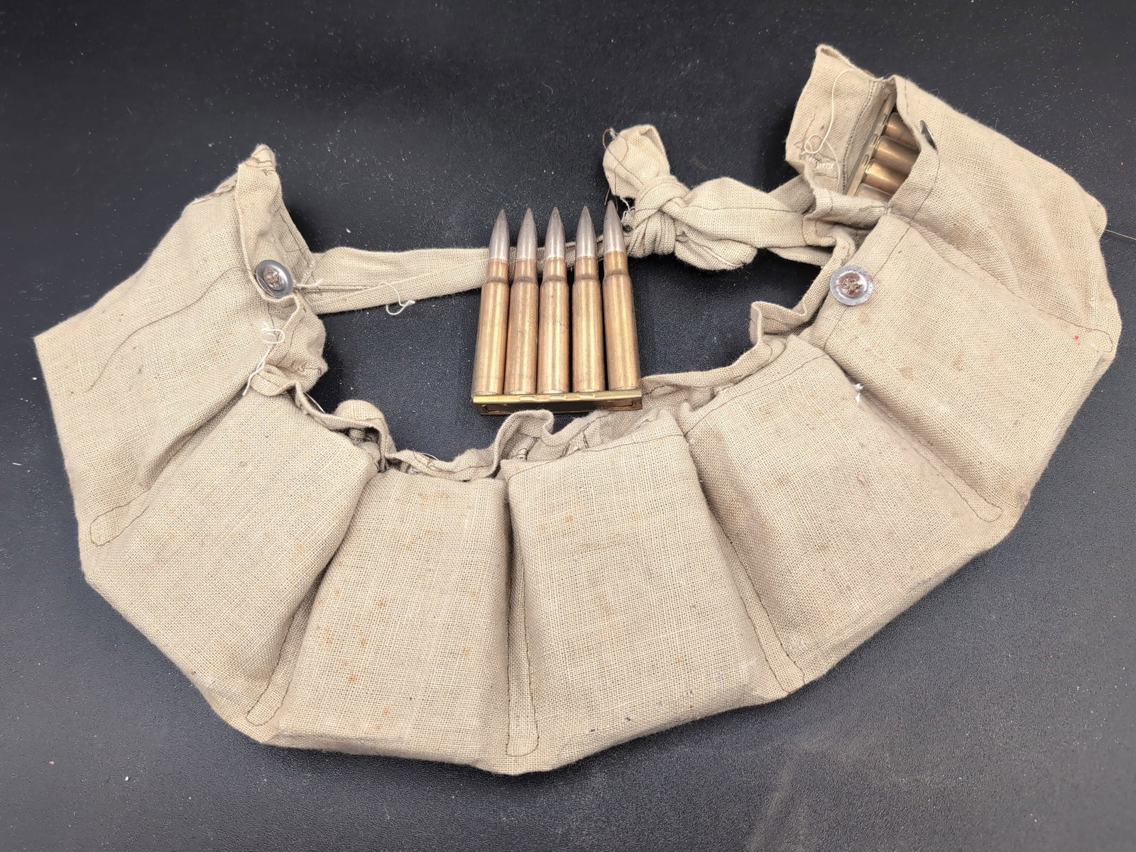 Canvas Ammunition Bandolier with Stripper Clips and Cartridges: A canvas ammunition bandolier featuring multiple storage pouches. The set includes several brass stripper clips loaded with cartridges. Headstamp markings on the cartridges include 'LIT', '1942', and 