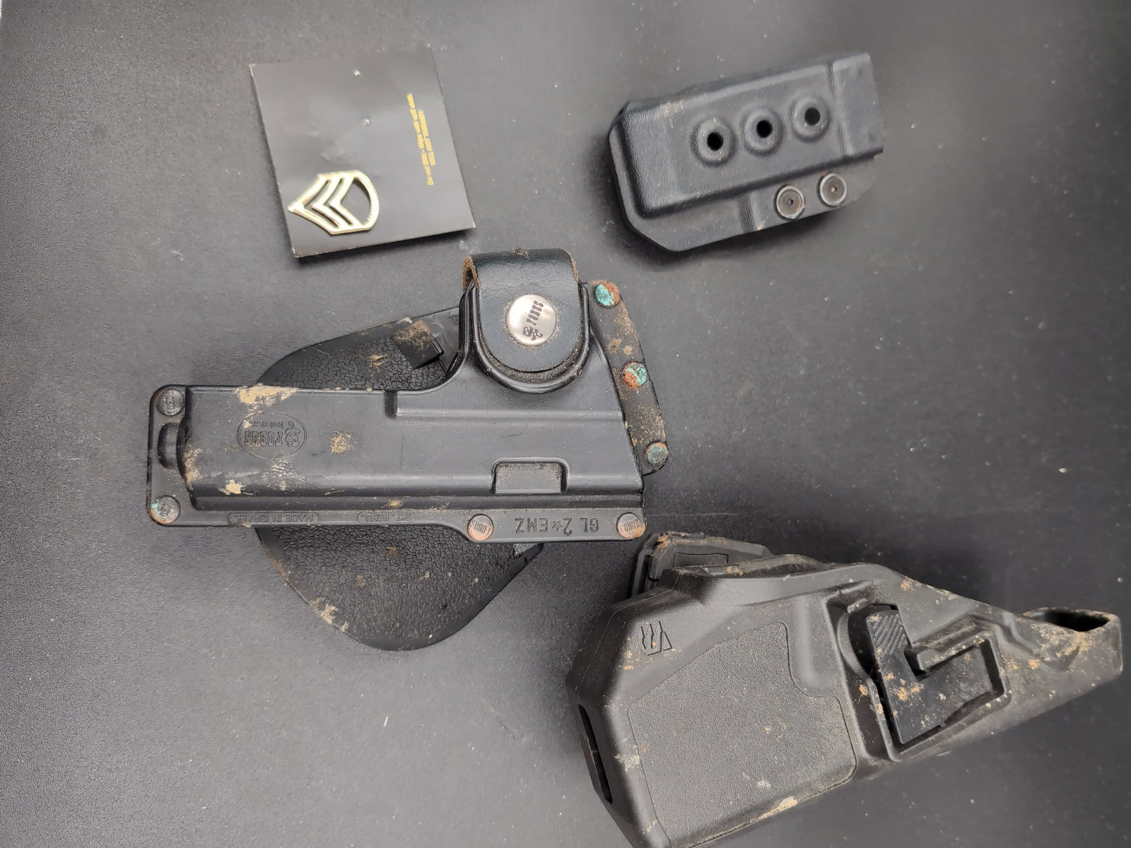 Fobus and Blackhawk Holster and Accessory Set: A collection of tactical gear including a Fobus GL 2 EMZ holster, a Blackhawk holster, an additional mounting component, and a metal rank insignia pin. The items are constructed from molded polymer an