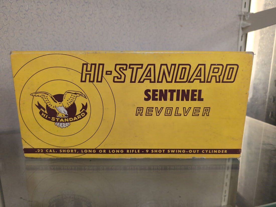 Hi-Standard Sentinel Revolver Box: A cardboard display box for a Hi-Standard Sentinel revolver, chambered for .22 caliber short, long, or long rifle ammunition. The box features a 9-shot swing-out cylinder design and includes internal 