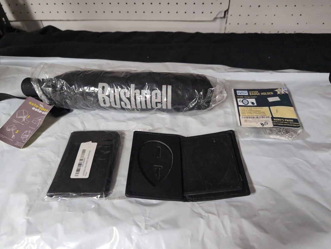 Bushnell Umbrella and Leather Badge Holder Assortment: This lot includes a Bushnell branded umbrella, a Hero's Pride universal oval leather badge holder (model #9140S) with metal chain and clip, and a LeatherBoss bifold wallet designed for badge storage. 