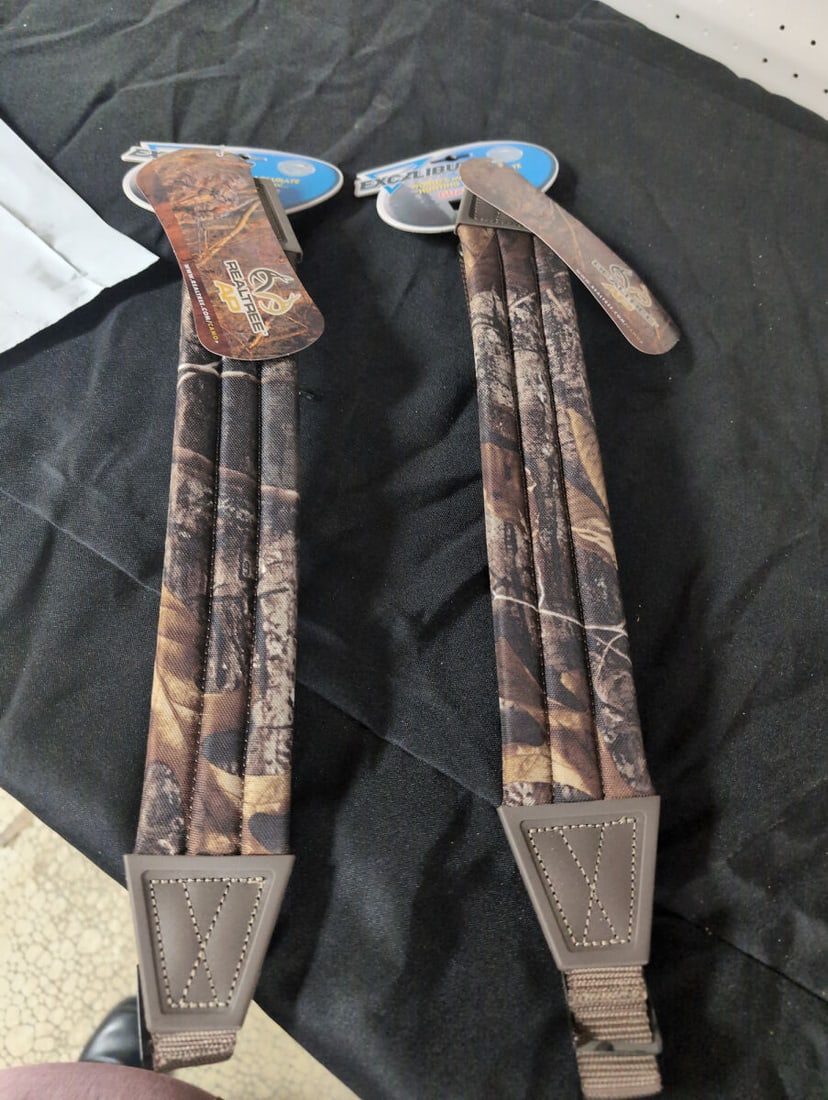 Excalibur Crossbow Realtree AP Camouflage Padded Slings: A pair of Excalibur Crossbow branded carrying slings featuring Realtree AP camouflage pattern. These padded slings include manufacturer hang tags and attachment hardware.