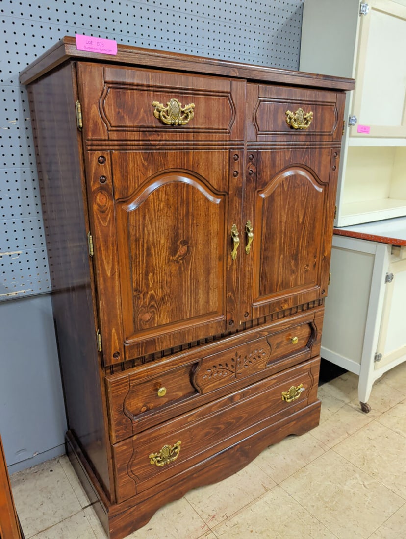 Wooden Armoire with Dual Doors and Lower Drawers: A wooden armoire featuring two upper cabinet doors that open to reveal interior shelving. The lower section includes two drawers with decorative brass-tone hardware and carved detailing on the upper d