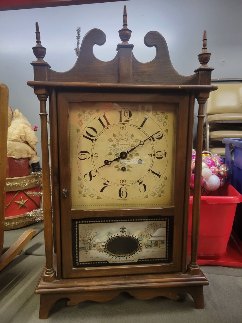 New England Clock Company Mantel Clock with Home t: A wooden mantel clock manufactured by the New England Clock Company, Farmington, Connecticut. The clock features a dial with floral motifs and a lower glass panel depicting a 'Home to Thanksgiving' wi