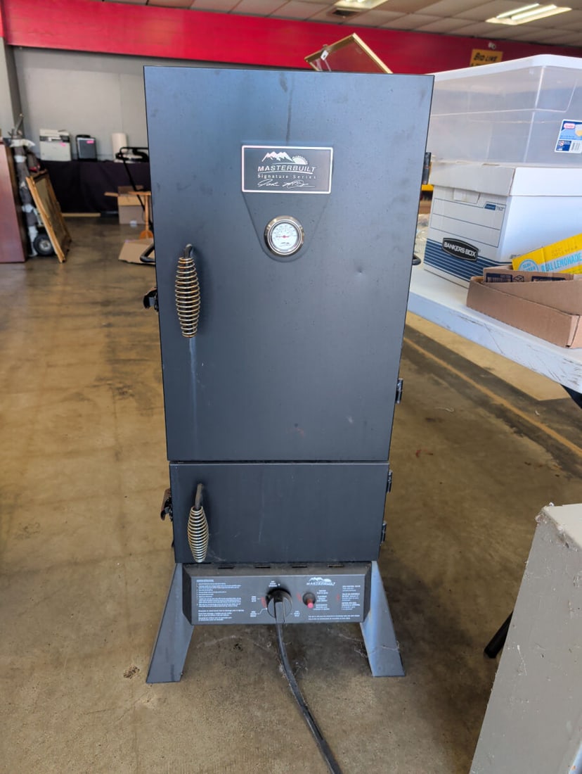 Masterbuilt Signature Series Propane Smoker: A Masterbuilt Signature Series vertical propane smoker featuring a front-mounted temperature gauge, dual-door design with spring handles, and an integrated control panel with ignition. The interior in