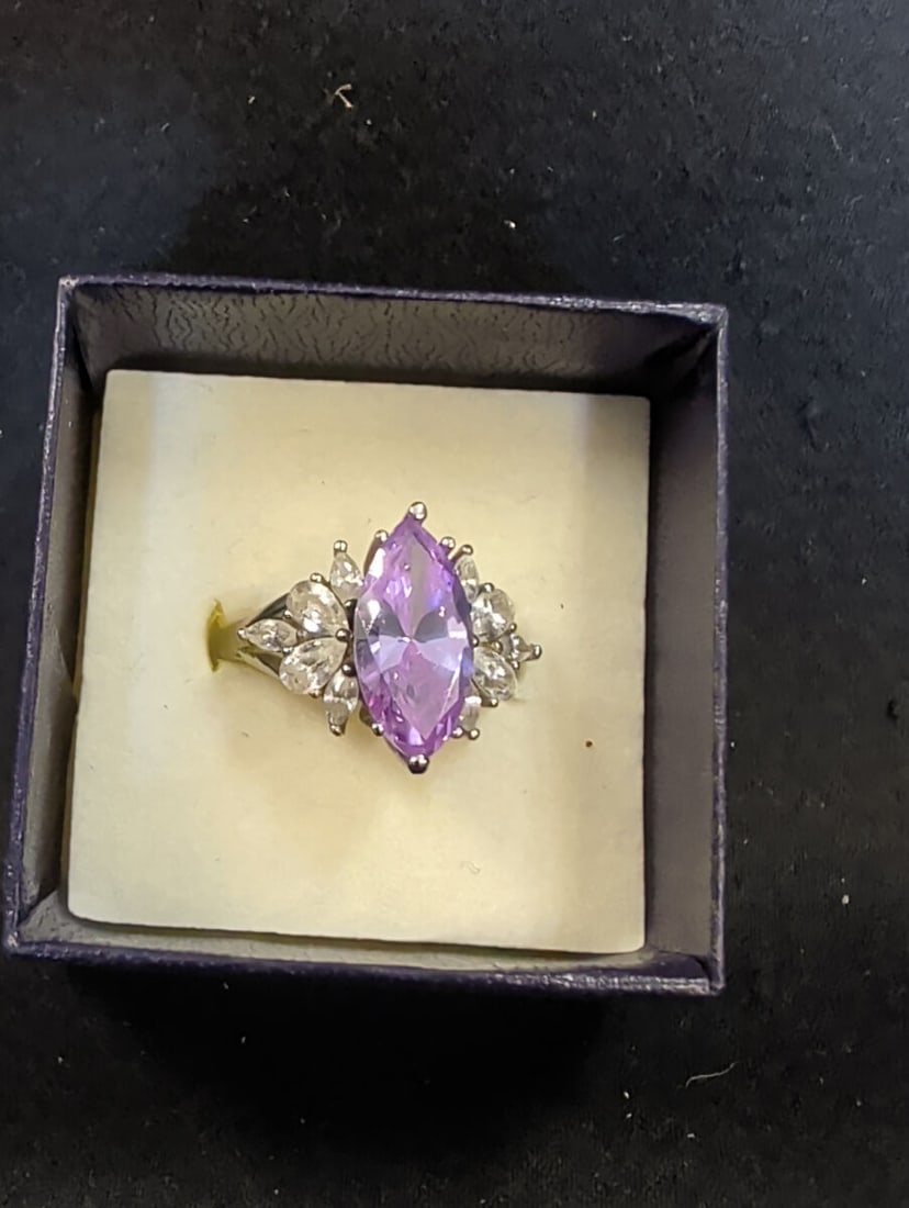 Sterling Silver Marquise Cut Purple Stone Ring wit: A ring featuring a central marquise-cut purple stone flanked by smaller clear accent stones. The band is marked as sterling silver. The item is presented in a small display box.