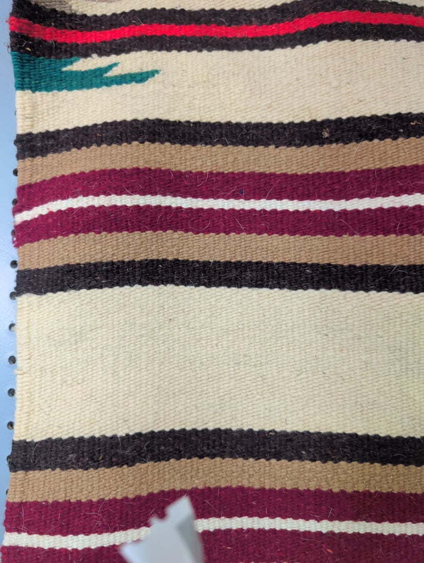 Navajo Woven Wool Rug 26 x 56 Inches: A hand-woven wool rug featuring a striped pattern in shades of cream, brown, maroon, and green. The textile measures 26 inches by 56 inches.