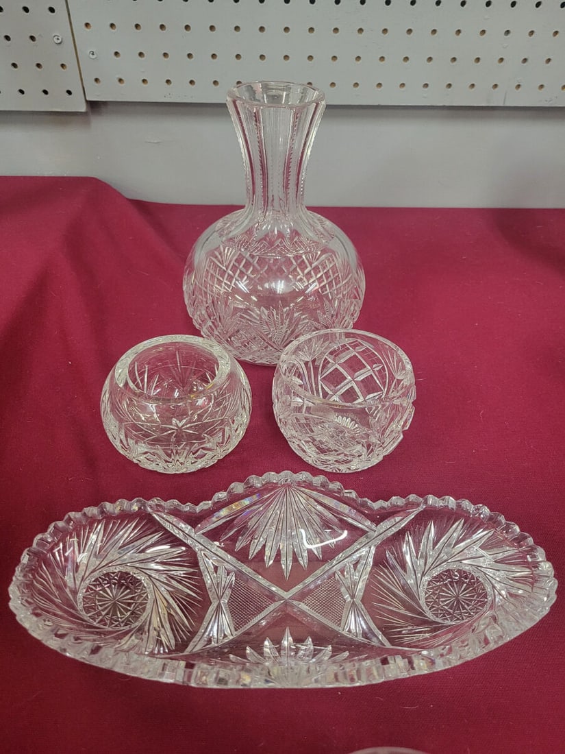 Cut Glass Decanter and Serving Set: A four-piece cut glass set featuring a decanter with a flared neck, two small bowls, and an elongated serving tray. Each piece is decorated with geometric and starburst patterns.