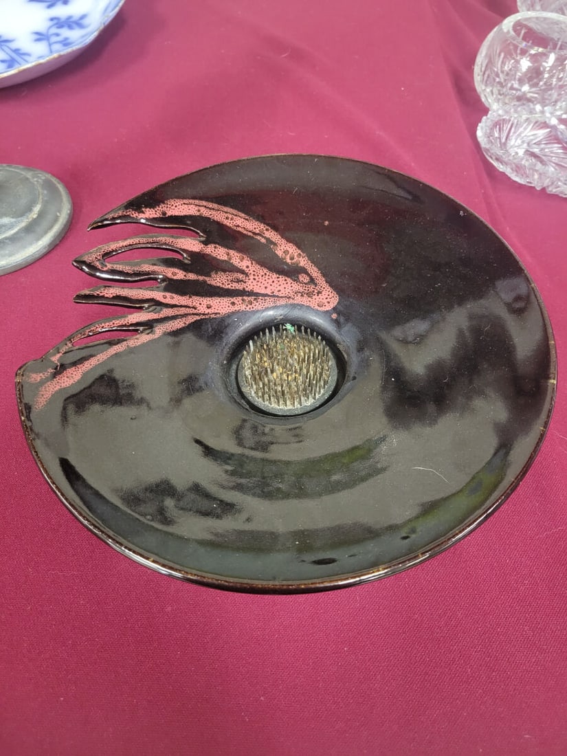 Studio Pottery Ikebana Flower Frog Bowl with Signe: A studio pottery bowl designed for floral arrangements, featuring a dark glaze with a textured, coral-colored accent detail. The center includes a metal pin-style flower frog. The underside of the bas