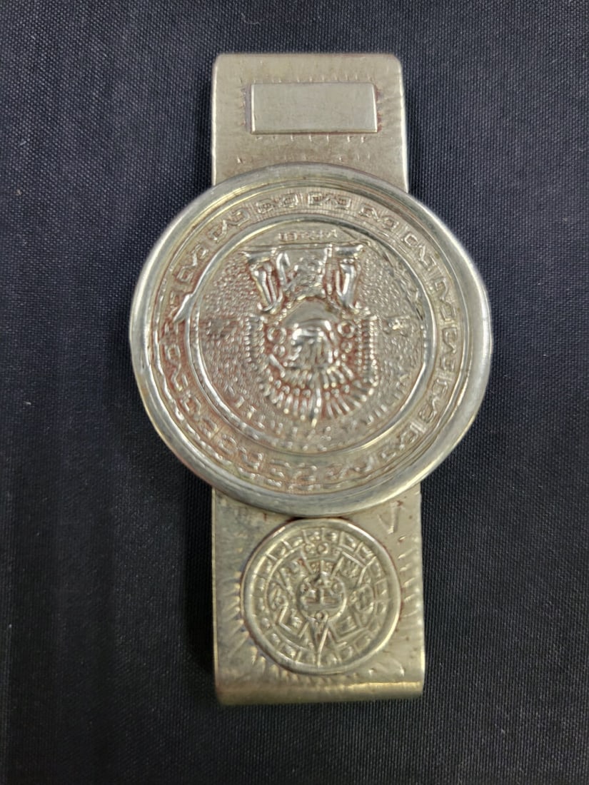 Mexican Sterling silver Aztec Calendar Motif Money: A metal money clip featuring a circular Aztec calendar design on the front. The reverse side bears a hallmark stamp reading Hecho en Mexico. The item measures approximately 2.5 inches in length.