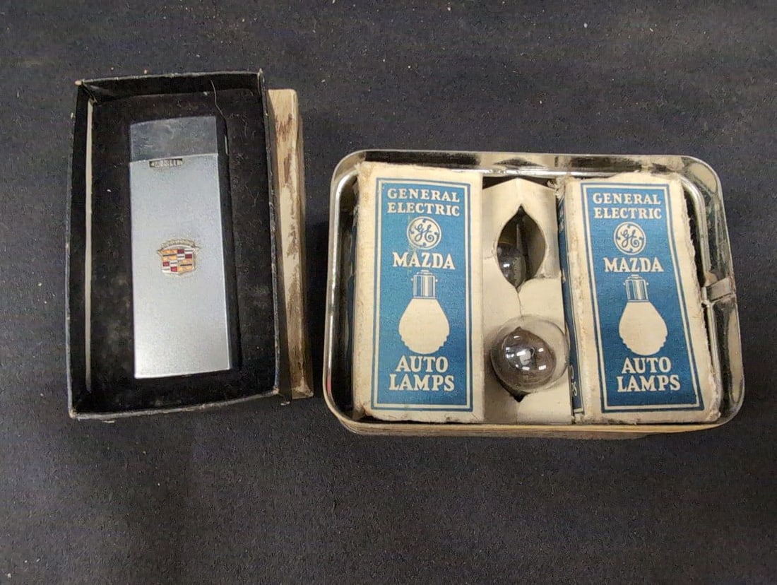Cadillac Bulb Kit Tin and Cadillac Crest Pocket Lighter in Box: Offering a pairing of Cadillac automotive memorabilia featuring a Cadillac Bulb Kit tin containing General Electric Mazda auto lamps and a Cadillac crest branded pocket lighter in its original present