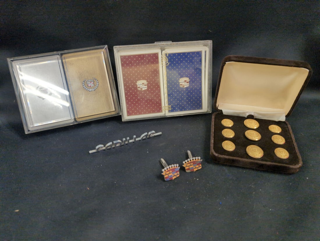 Assorted Cadillac Automotive Memorabilia and Accessories Collection: Collection of Cadillac themed items including two sets of playing cards in plastic cases, a boxed set of gold toned blazer buttons, enameled crest cufflinks, and a metal Cadillac script emblem.
