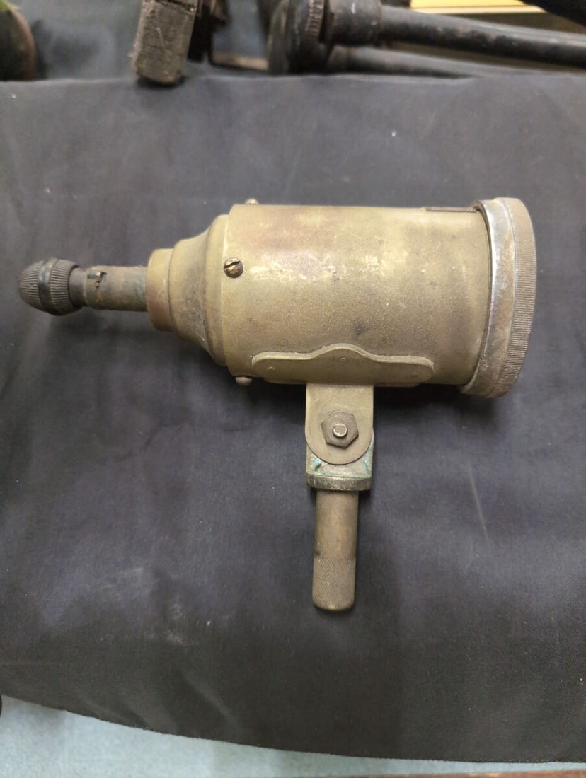 Dirigible spotlight: A brass spotlight featuring a rounded housing, an adjustable mounting bracket, and a convex glass lens at the front. The piece includes adjustment knobs at the rear and along the mounting stem, showin
