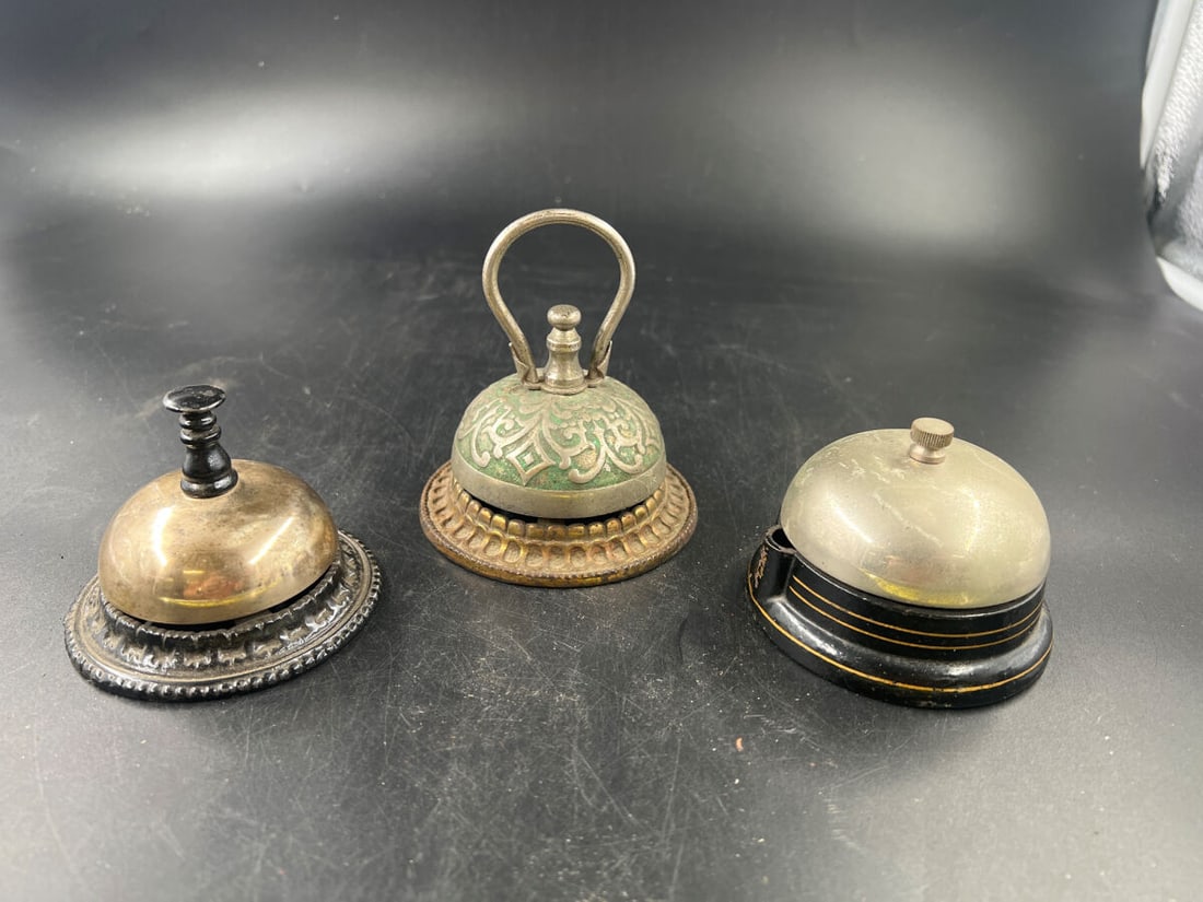 Collection of Three Assorted Call and Desk Bells Including Electric and Mechanical Models: Collection of three assorted call and desk bells featuring varied designs and mechanisms. The lot includes a mechanical bell with a dark metal base and plunger, an ornate bell with a patterned green a