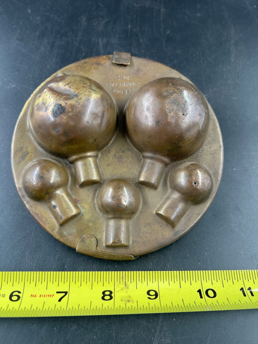 The Atlantic Bulb Box Brass Mold: The Atlantic Bulb Pot hinged brass mold featuring embossed lettering on the exterior and interior cavities designed for shaping spherical forms with stems. Measures approximately seven inches in diame