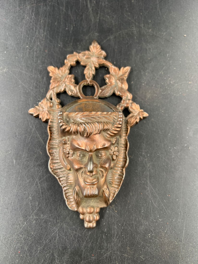 Cast Metal Green Man Match Holder Wall Mount: Cast metal match holder featuring a detailed Green Man or pan-like face motif with grapevine and leaf accents. Includes an integrated hanging loop and stamped inventory number 589 on the reverse. Disp