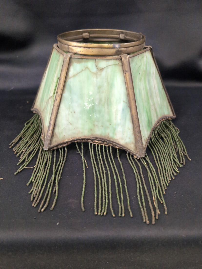 Slag Glass Lamp Shade with Metal Frame and Beaded Fringe: Green and white slag glass lamp shade featuring a hexagonal metal frame construction and a hanging green beaded fringe along the lower border. Note the presence of cracks and fractures in one of the g