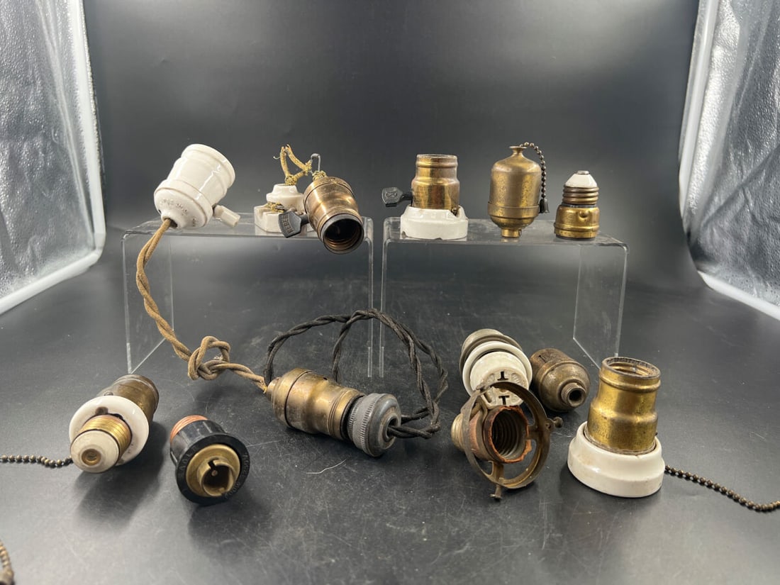 Collection of early Electrical Lamp Sockets and Adapters: A diverse grouping of electrical components, featuring various brass, porcelain, and bakelite lamp sockets, pull-chain mechanisms, and specialized adapters. Several pieces include remnants of twisted 