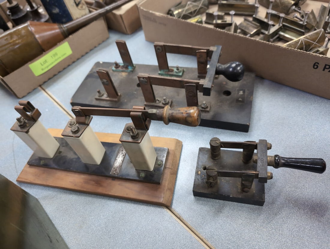 Collection of Three Industrial Knife Switches with Ceramic Insulators and Wooden Bases: Collection of three heavy-duty industrial electrical knife switches mounted on wooden and insulated bases, featuring brass components, copper blades, and wooden or Bakelite handles. One switch include