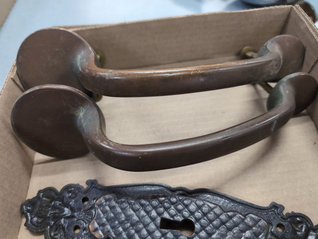 Antique Hardware Lot with Metal Door Pull Handles and Ornate Escutcheon Plates: This lot includes a pair of large bronze-toned metal door pull handles alongside two decorative cast metal backplates, one featuring a keyhole cutout. The escutcheon plates display a textured diamond 