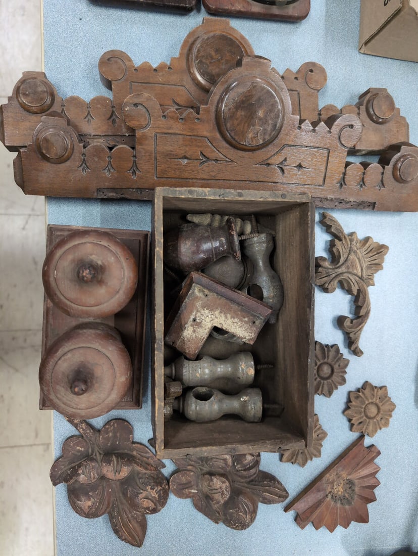 Eastlake Architectural Wooden Carvings, Finials, and Moldings: Collection of assorted wooden architectural elements including carved floral appliques, leaf motifs, decorative finials, crown molding pieces, and turned wooden components housed partially in a wooden
