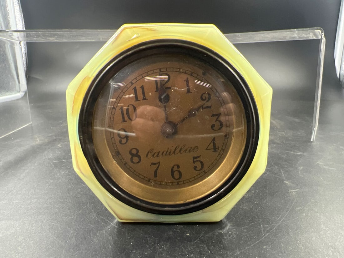Cadillac Slag Glass Electric Desk Clock: Featuring a slag glass housing with marbled yellow and blue tones, this electric desk clock includes a round face marked with the Cadillac name. The back panel includes operating instructions and oper
