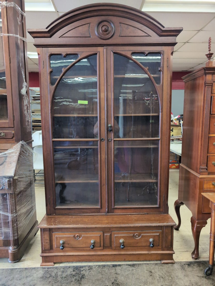 Large Walnut Bookcase with Glass Doors and Base Drawers: Large wooden bookcase featuring an arched top cornice, two glass-paneled cabinet doors with decorative wooden tracery, and adjustable interior shelving. The lower section includes a flat surface step-