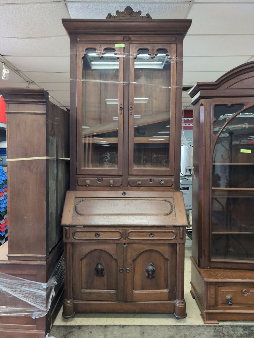 Large Walnut Minerva Head Secretary Desk with Glass Display Top and Carved Cabinet Doors: Large wooden secretary desk featuring an upper glass-paneled display hutch with shelving, a drop-down writing surface revealing interior cubbies and small drawers, and lower cabinet storage doors