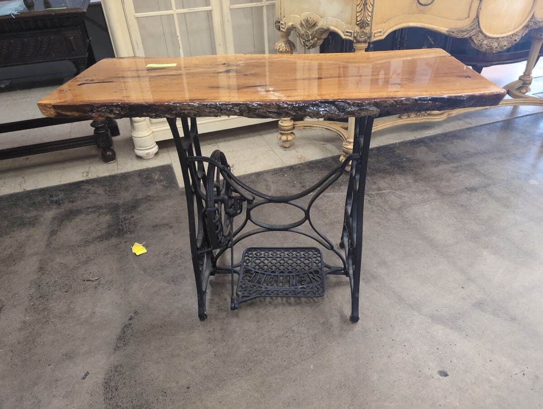 Live Edge Wooden Top Table with Cast Iron New Home Treadle Base: Custom accent table featuring a finished live edge wooden top with natural grain patterns and knots, paired with a repurposed cast iron New Home treadle sewing machine base complete with foot pedal an