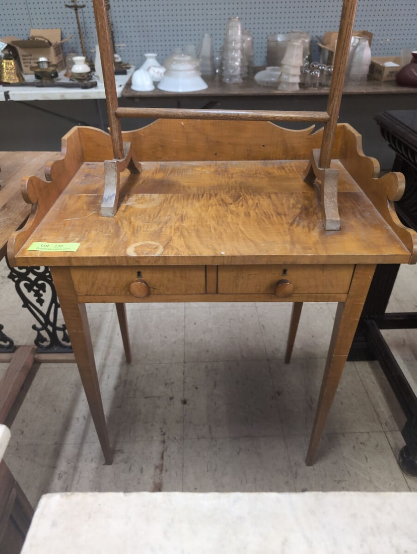 Tiger Maple Washstand: Wooden washstand crafted from tiger maple, featuring a scalloped gallery splash guard, two lower drawers with wooden pulls and keyholes, tapered legs. Shows visible surface wear and staining consisten